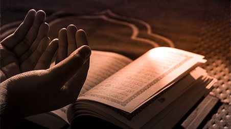 Hands in prayer over an open book